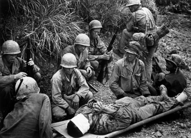 Mayo de 1945 en Okinawa. Un soldado de la 7ª inf. Div. Quien aparentemente fue herido en la cabeza y el pie yace en una camilla con sus compañeros a su alrededor